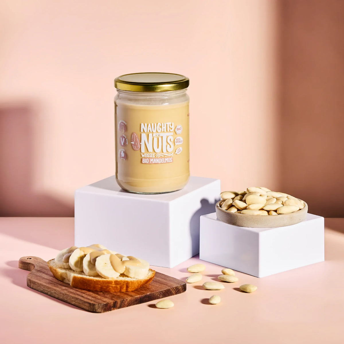 Bio Weisses Mandelmus im Glas auf einem Podest mit Bananenbrot und Mandeln