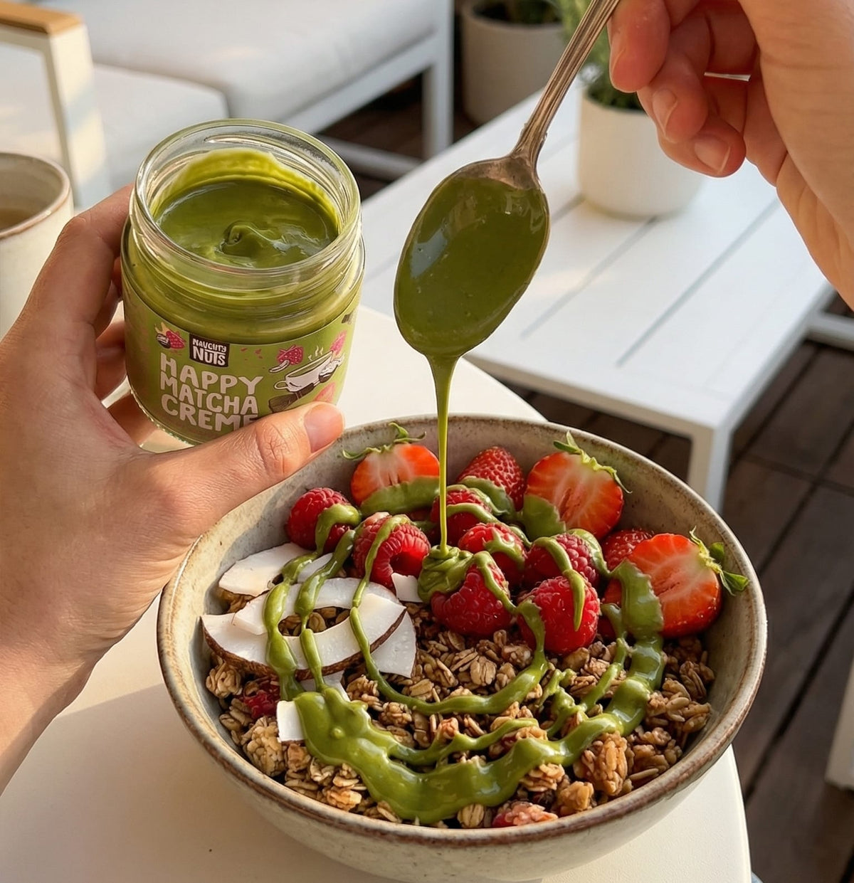Happy Matcha Creme wird aus einem Glas auf eine Schale mit Müsli, Beeren und Kokosnuss geträufelt