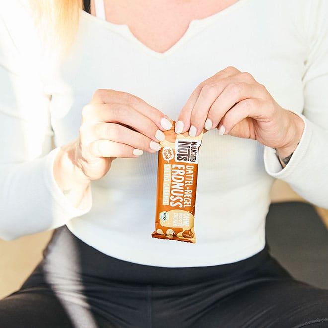Hände öffnen einen Bio Dattel-Riegel Erdnuss Salted Caramel