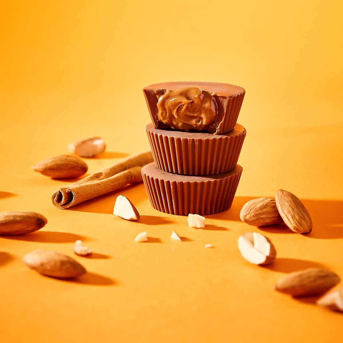 Gestapelte Bio-Mandelbutter-Cups Zimtschnecke mit Mandeln und Zimtstangen auf orangefarbenem Hintergrund