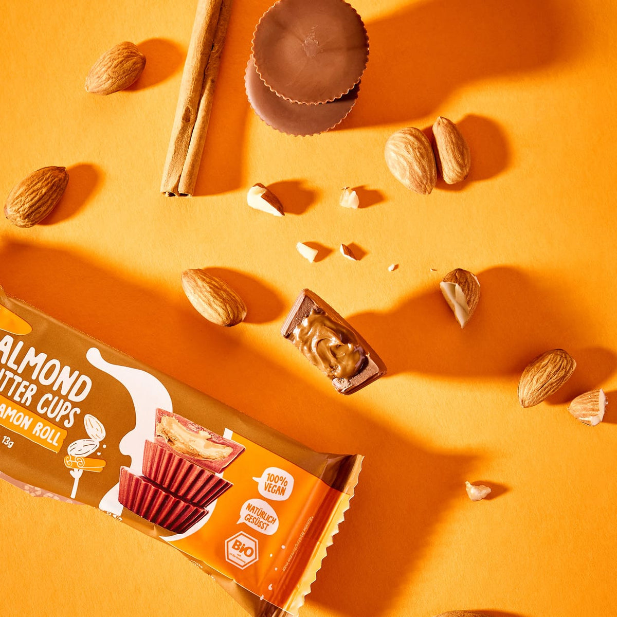 Bio Almondbutter Cups Cinnamon Roll mit Mandeln und Zimtstangen auf orangefarbenem Hintergrund