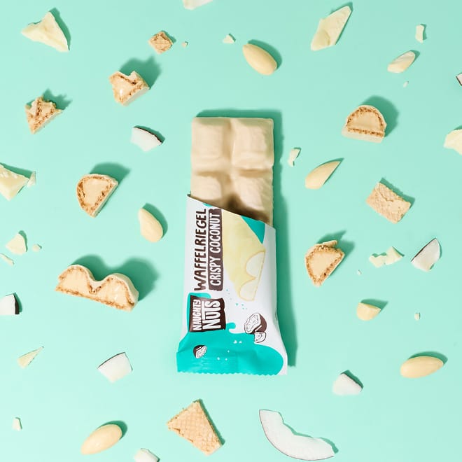Bio Schoko-Waffelriegel Crispy Coconut auf blauem Hintergrund mit Kokosnussstücken und Mandeln