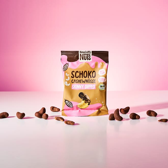 Naughty Nuts Schoko Cashewnüsse Skinny Dipped Packung mit verstreuten Nüssen