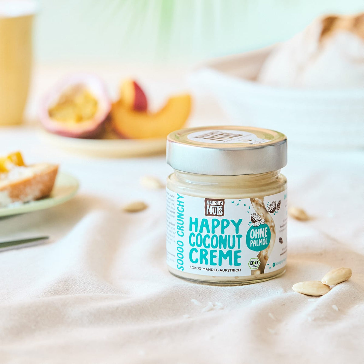 Happy Coconut Creme Glas auf Stoff mit Früchten im Hintergrund