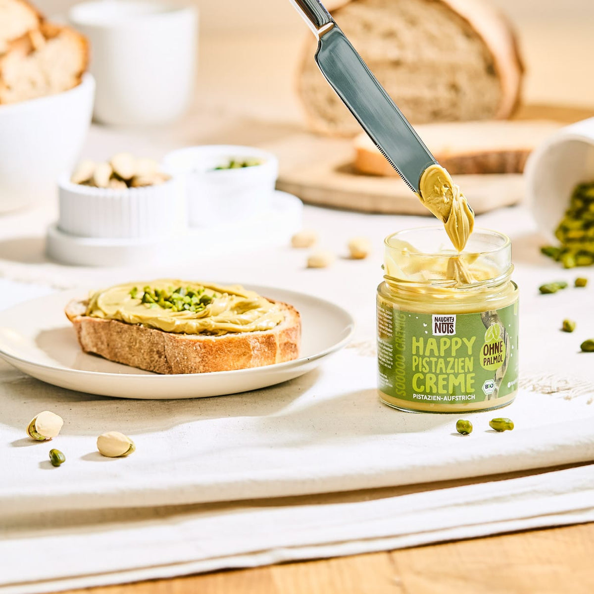 Messer mit Pistaziencreme über einem Glas Happy Pistazien Creme und einem Toast mit Aufstrich