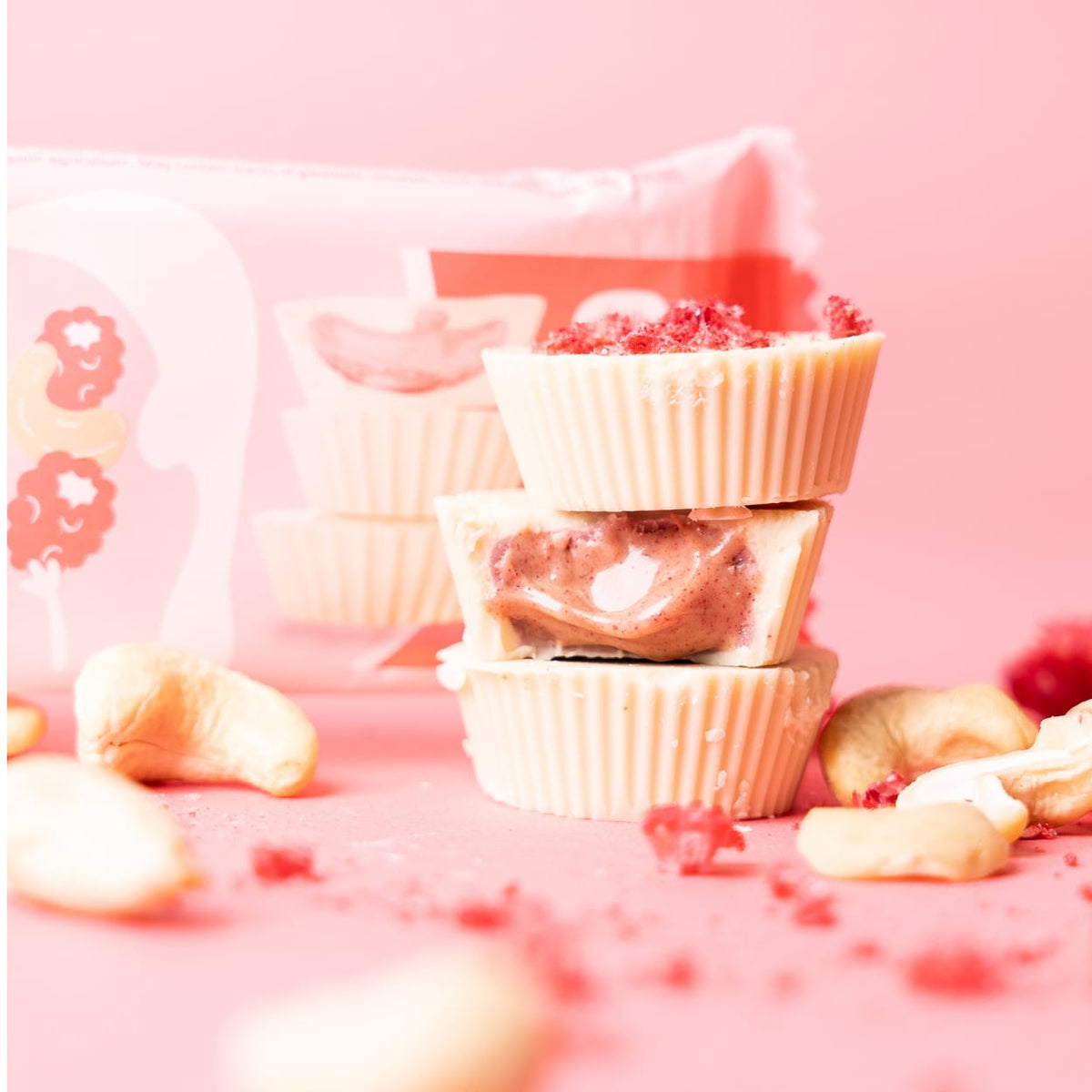 Bio Nutbutter Cups Mixed Box mit Cashewkernen und Himbeerstückchen auf rosa Hintergrund